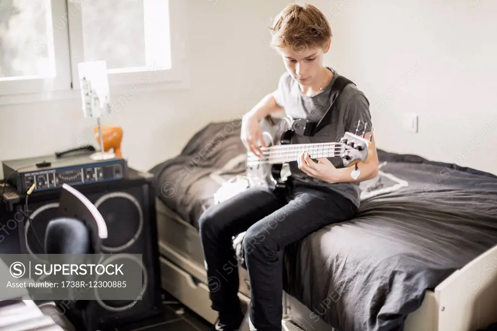 Teenage boy playing a guitar on bed