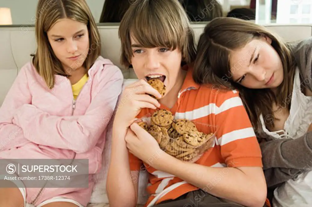Boy eating chocolate cookies with two girls beside him