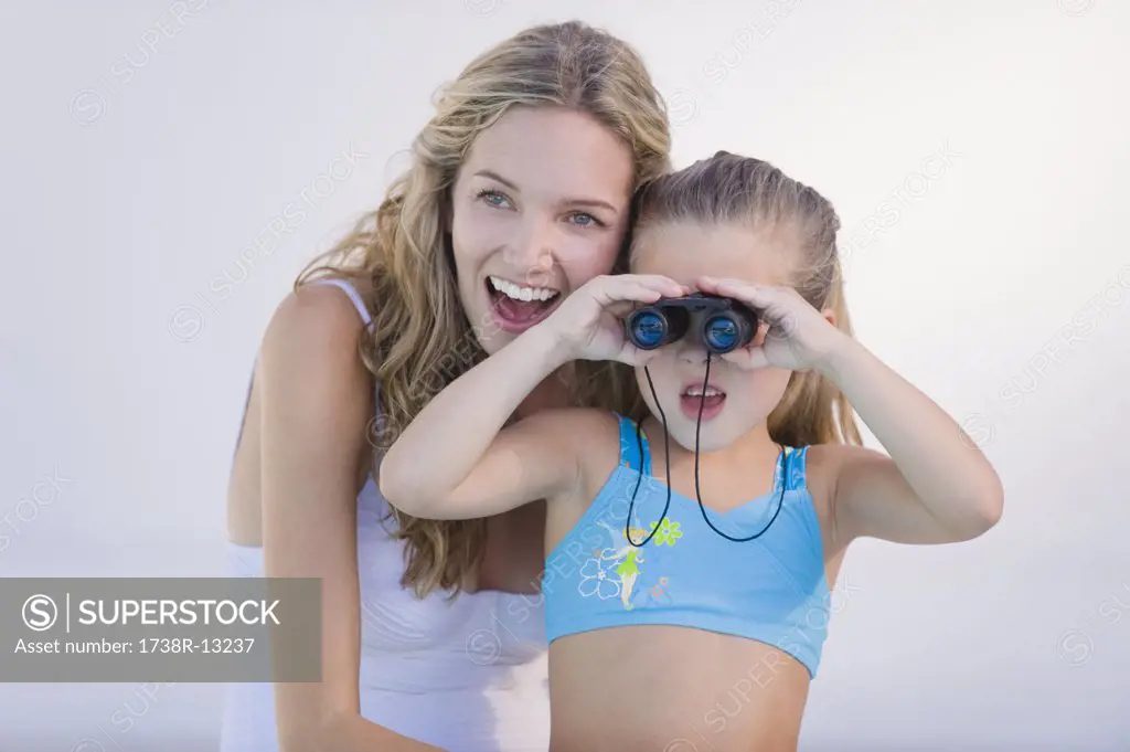 Girl looking through binoculars with her mother laughing