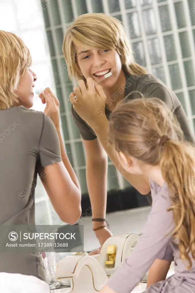 Teenage boy brushing his teeth with his sister looking at him