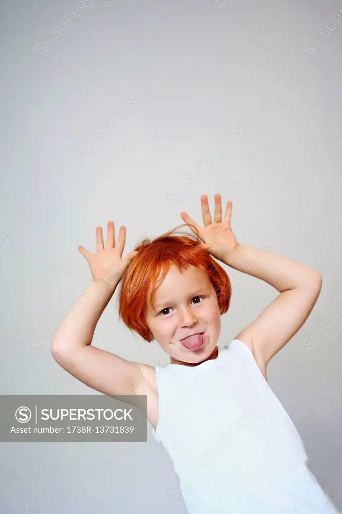 Portrait of a red-haired little girl indoors sticking her tongue out and putting her hands in the air