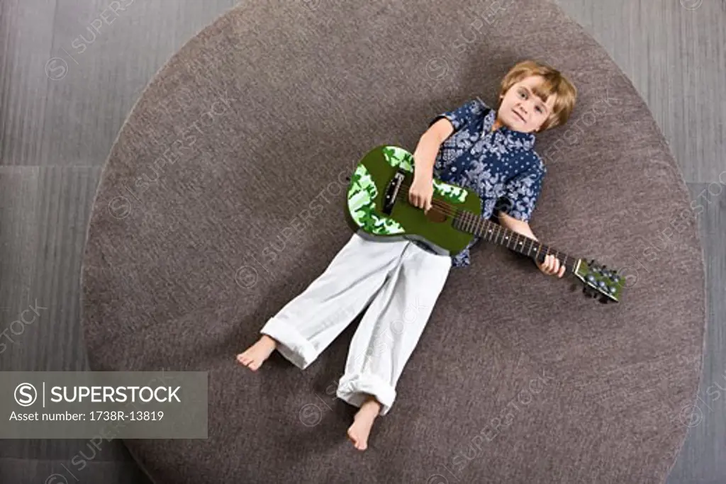 Boy lying on a round sofa and playing a guitar