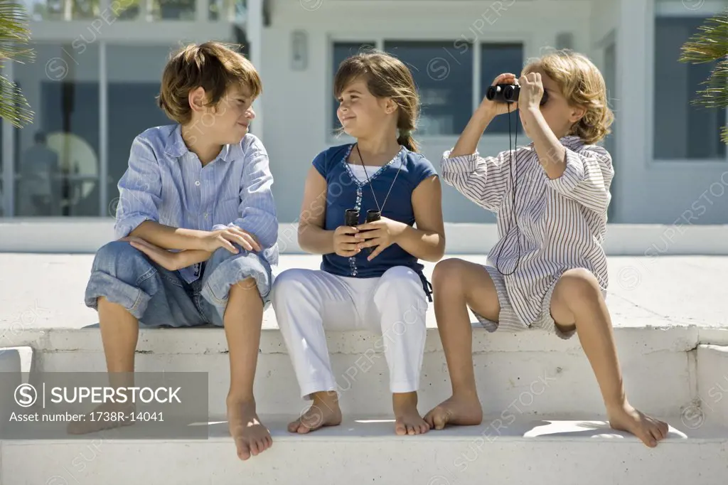 Boy looking through binoculars with his friends sitting beside him