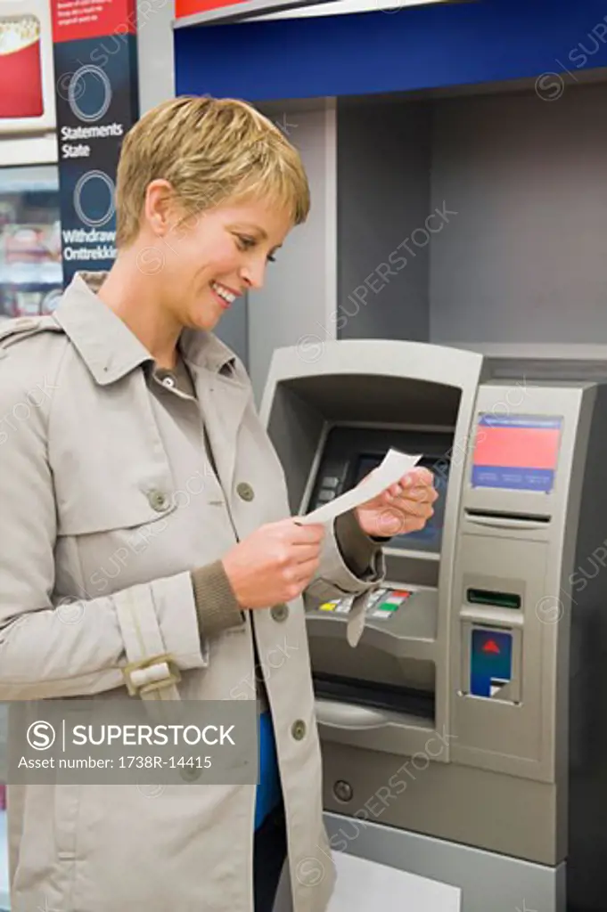 Woman reading a transaction slip at an ATM and smiling
