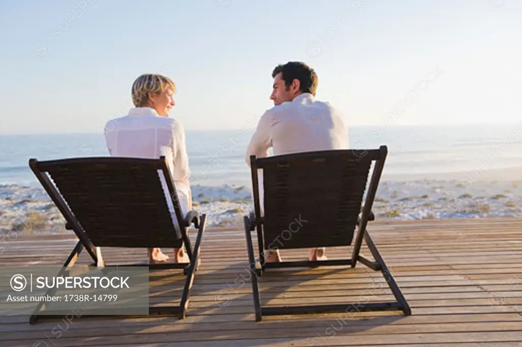 Couple sitting on deck chairs on the beach