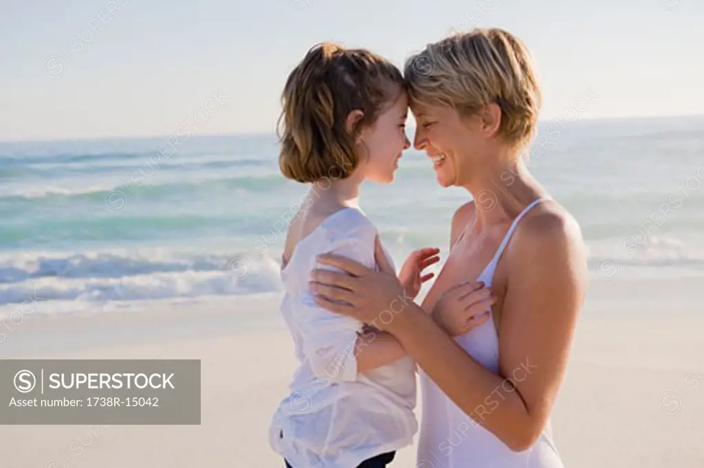 Woman with her daughter rubbing noses on the beach