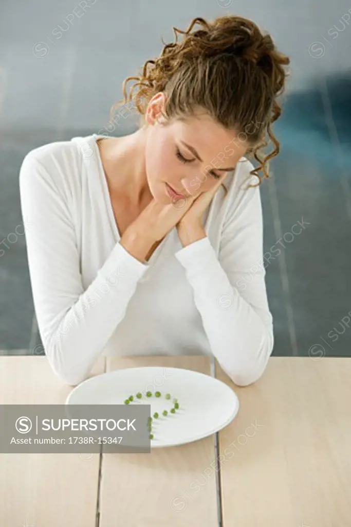 Woman sitting at a table with peas in question mark shape on a plate