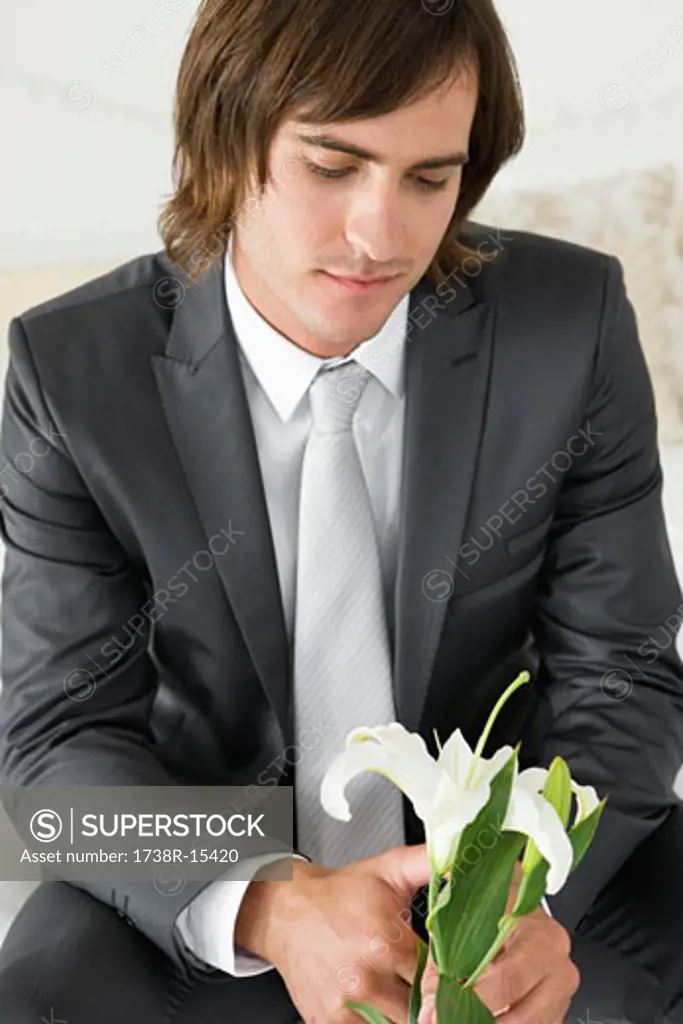 Groom sitting on the bed and holding a lily flower