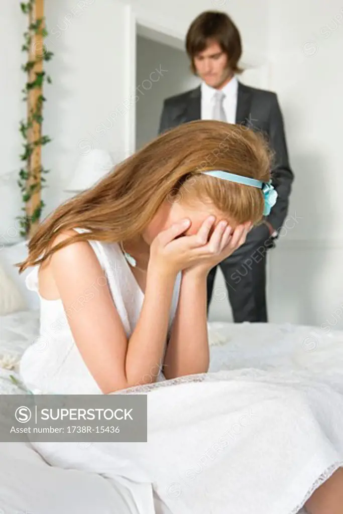 Disappointed girl sitting on bed and a groom standing near her