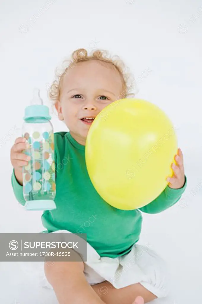Baby boy holding a balloon and a baby bottle