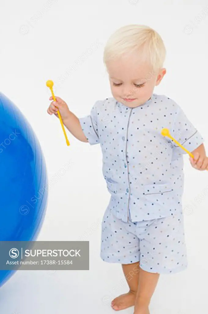 Baby boy holding xylophone mallets and standing near a fitness ball