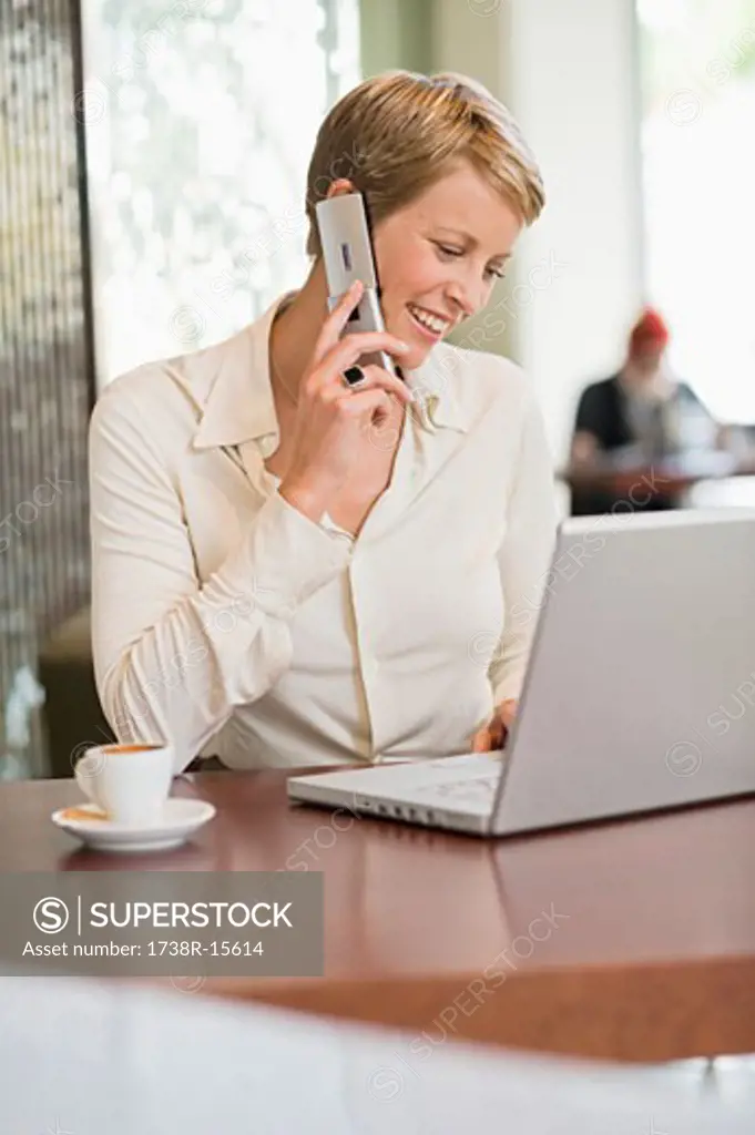 Businesswoman talking on a mobile phone and looking at a laptop