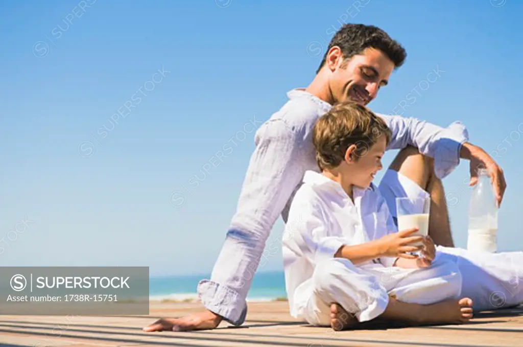 Man and his son drinking milk on the beach