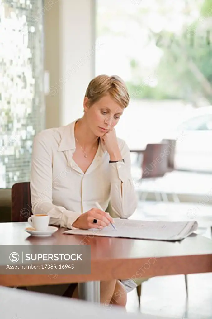 Businesswoman sitting in a restaurant and reading a financial newspaper