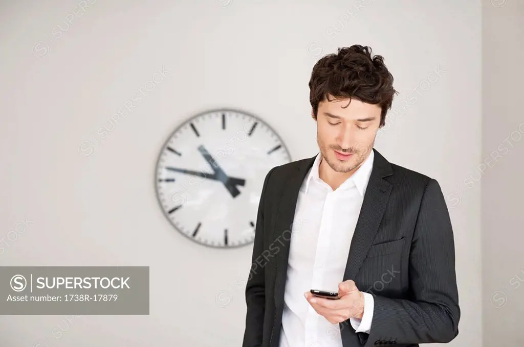 Businessman standing in front of a clock and using a mobile phone