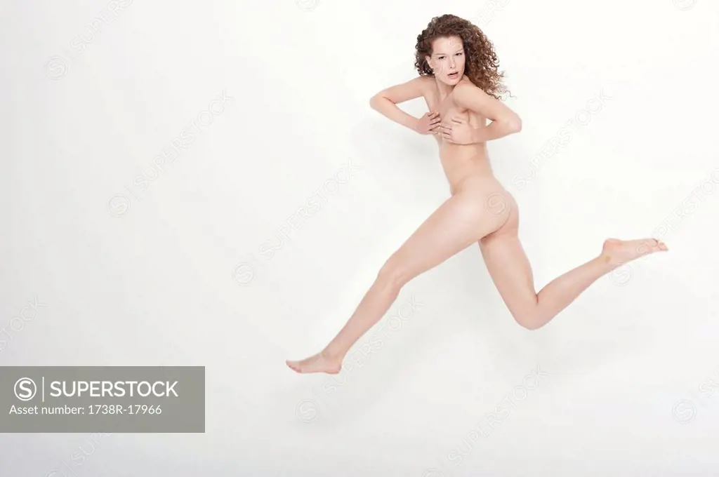 Naked woman covering her breasts and jumping