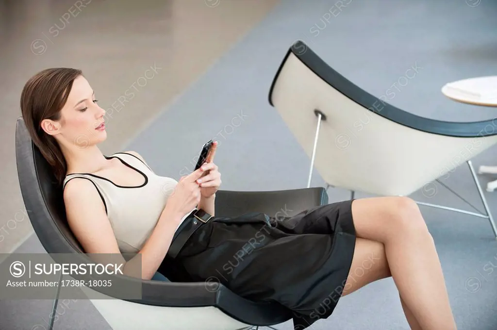 Woman reclining in a chair and text messaging with a mobile phone