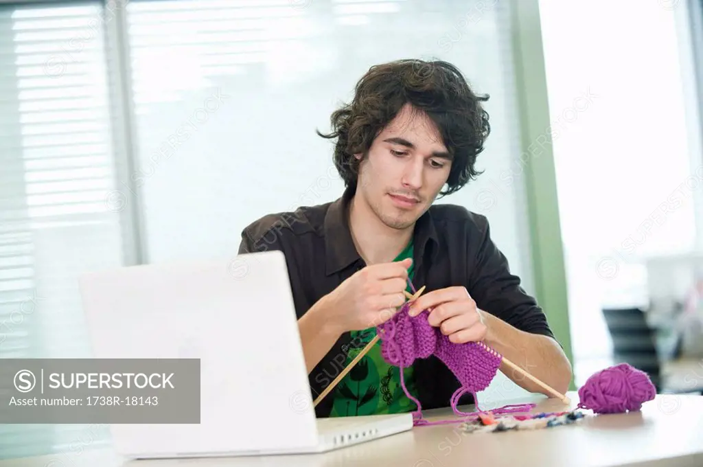 Businessman knitting in front of a laptop