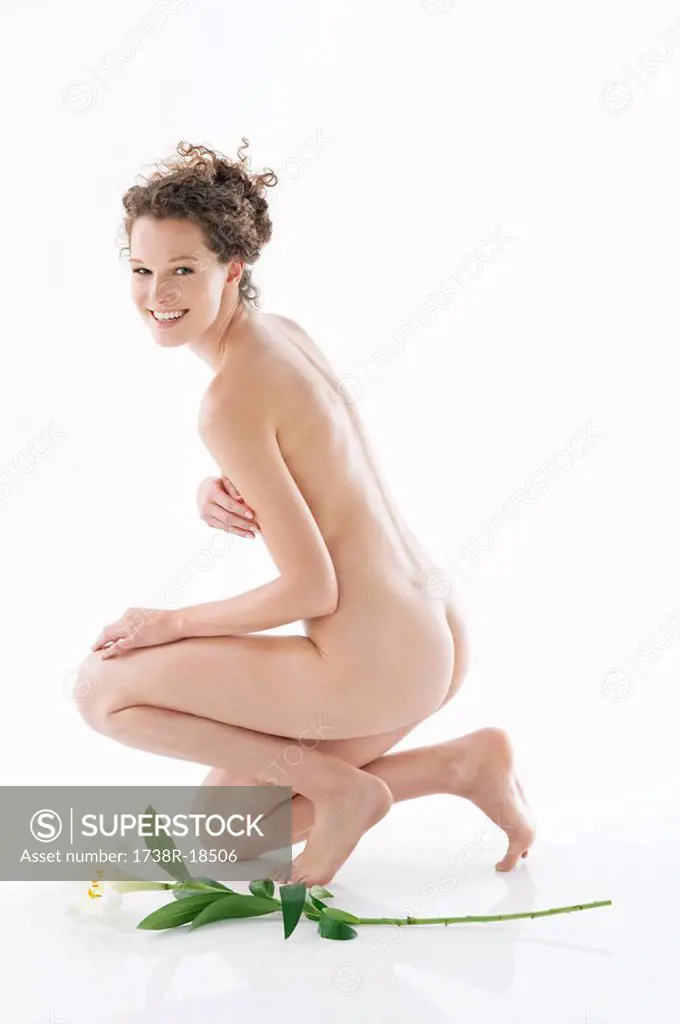 Naked woman kneeling beside a flower and smiling