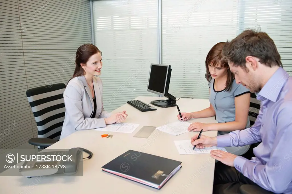 Couple signing agreement form in a real estate agent´s office