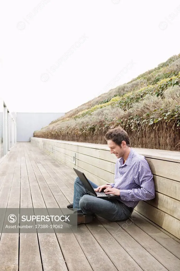 Man using a laptop on a boardwalk