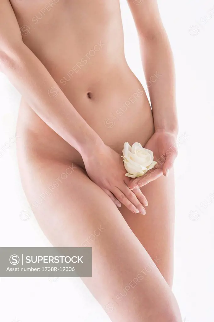 Mid section view of a naked woman covering groin with a rose