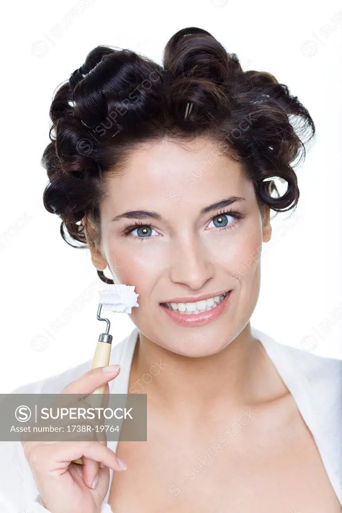 Young woman with hair clips, using facial massage roller