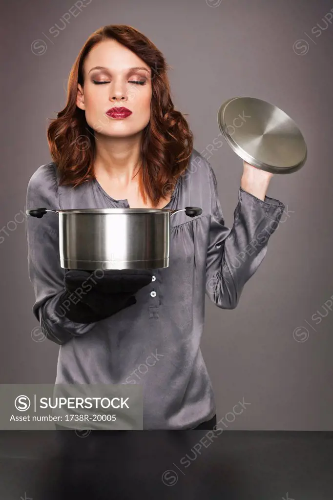 Young woman smelling aroma from stew pot