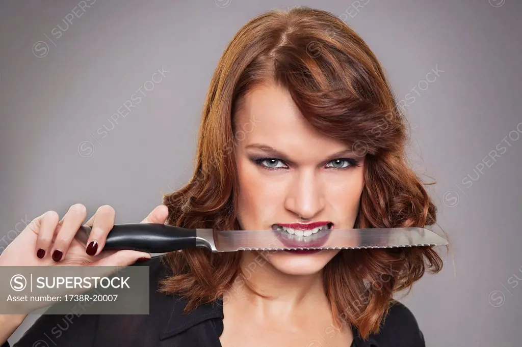 Young woman with knife between teeth