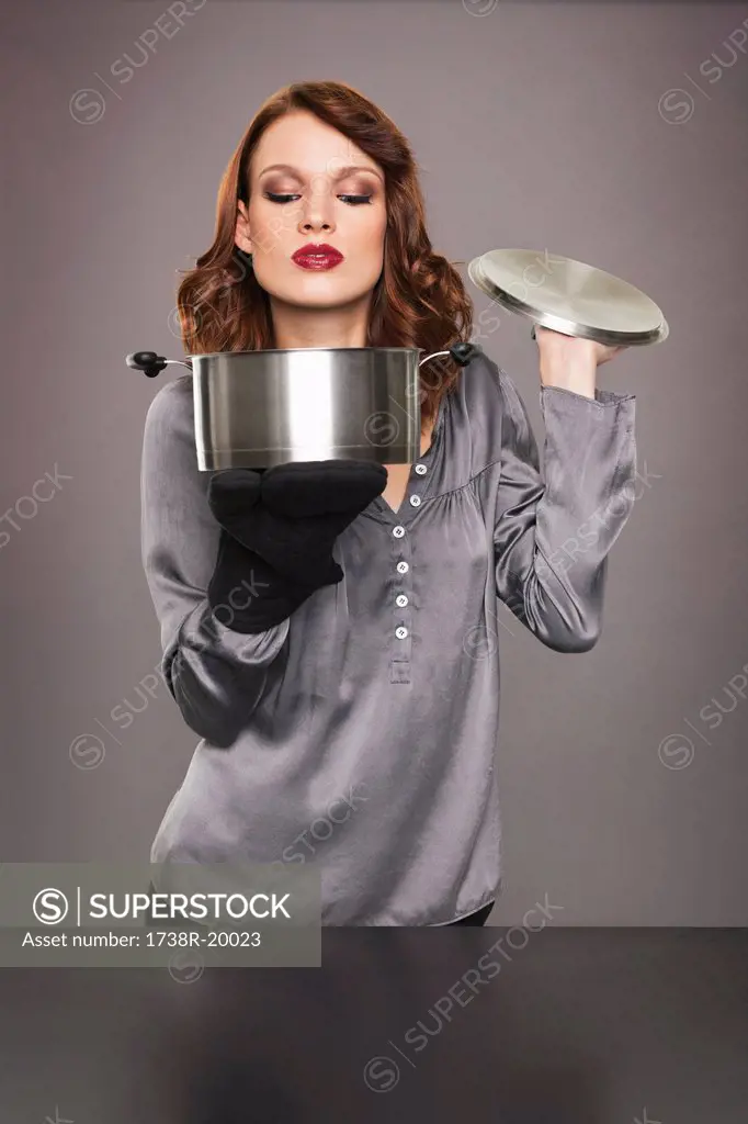 Young woman smelling aroma from stew pot