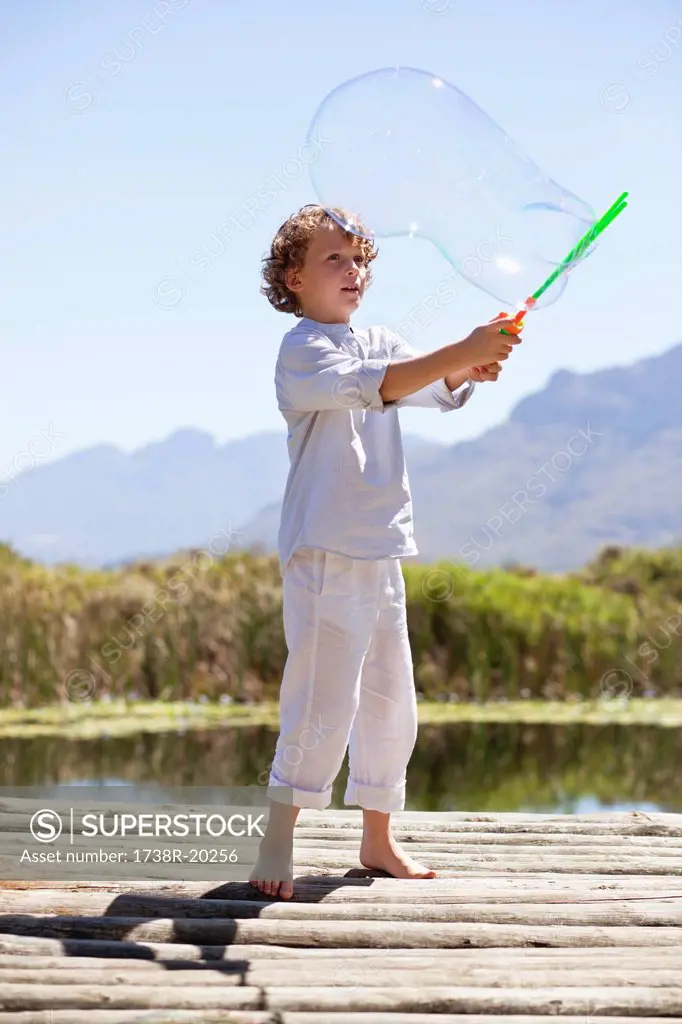 Boy playing with a bubble wand at a pier