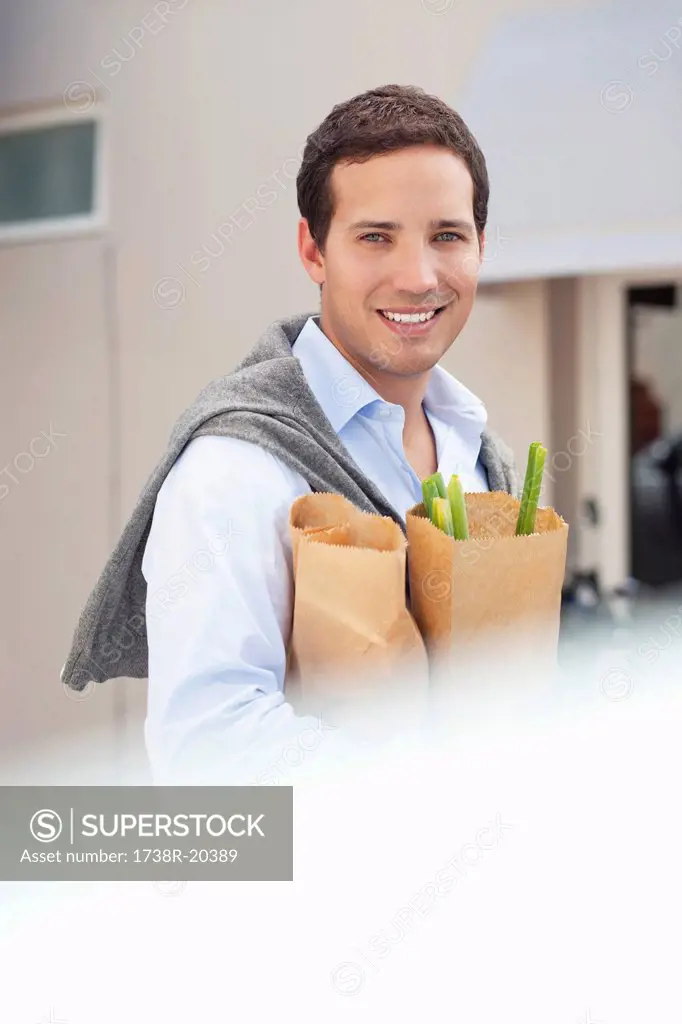Portrait of a mid adult man holding paper bags full of vegetables and smiling