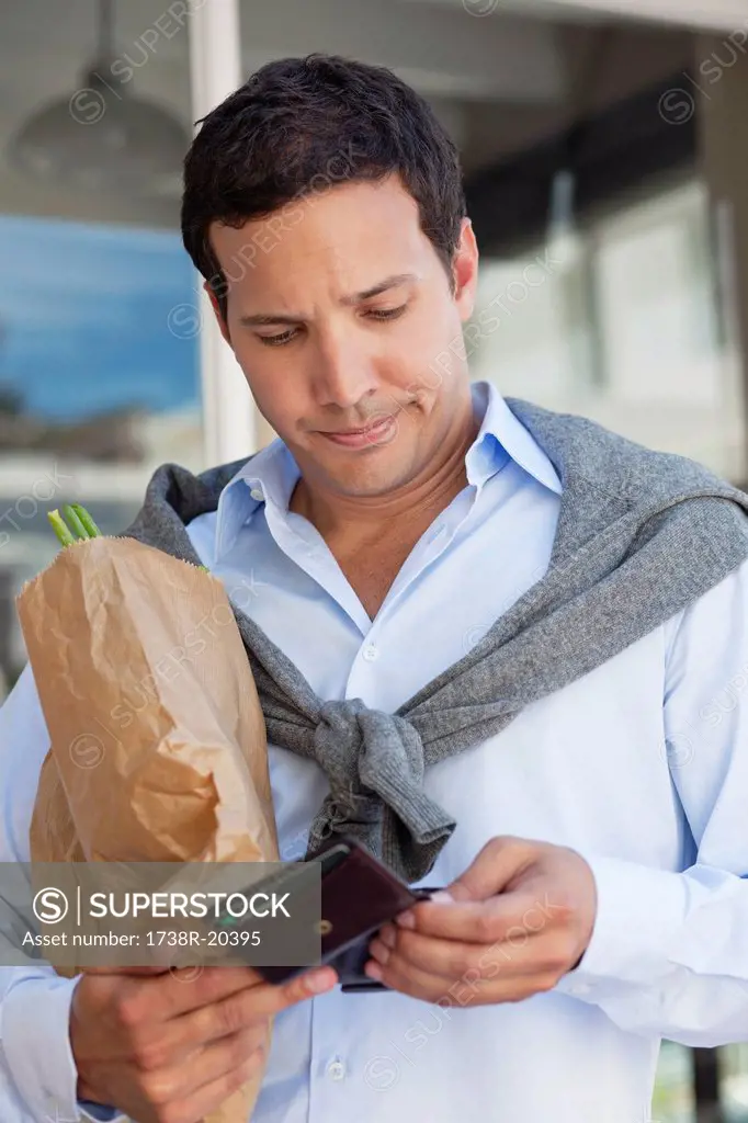 Mid adult man checking the empty wallet with paper bag full of vegetables