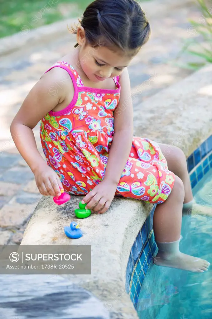 Girl playing with rubber ducks at the edge of swimming pool