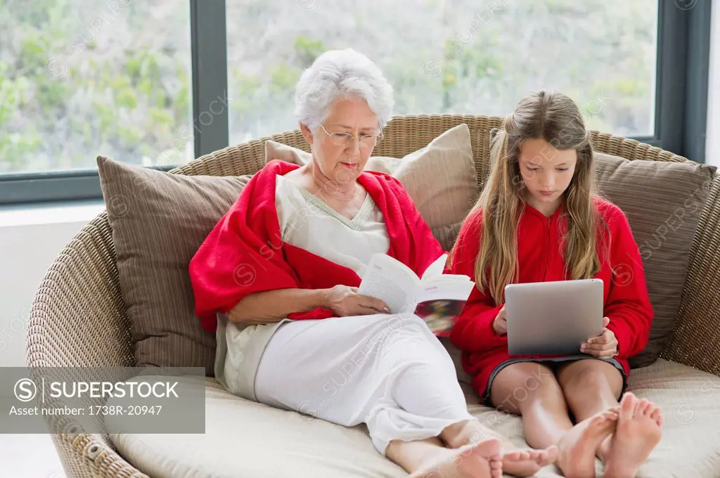 Senior woman reading a magazine with her granddaughter using a digital tablet