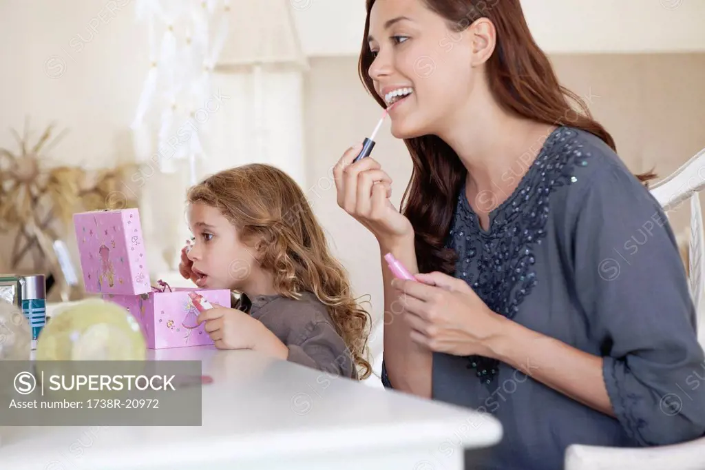 Young woman and little girl applying make_up at dressing table