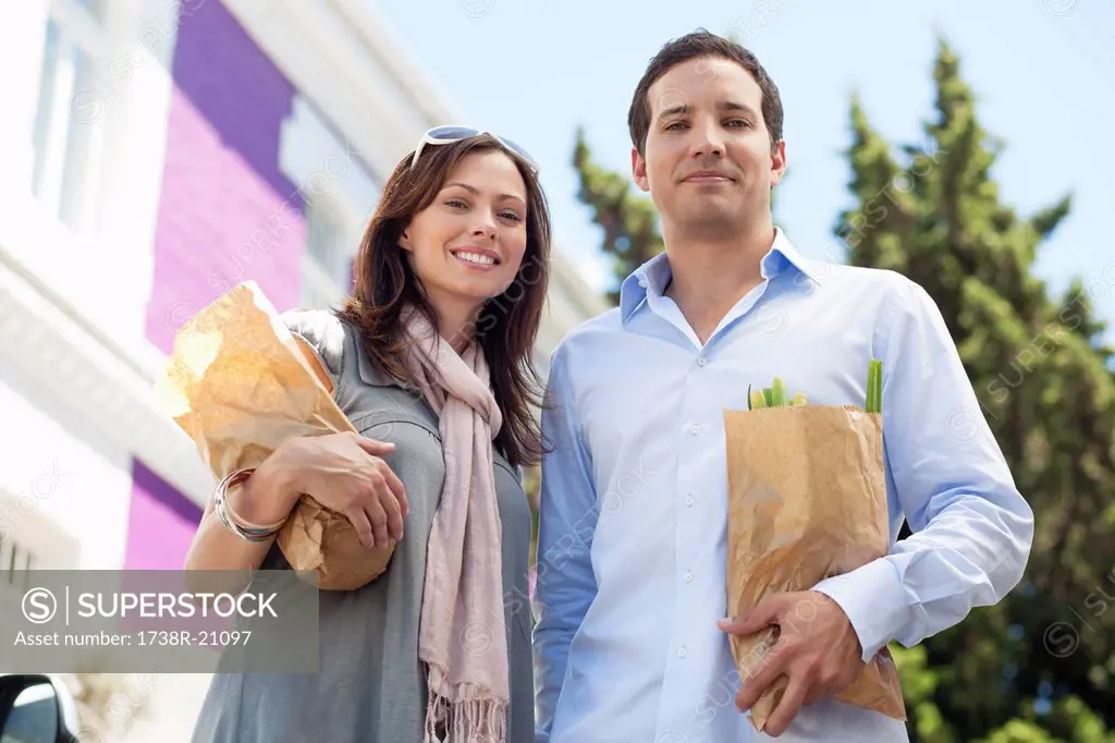 Portrait of a couple standing with paper bags full of vegetables