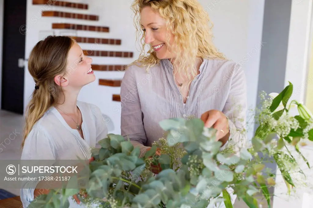 Mid adult woman and her daughter touching leaves and smiling