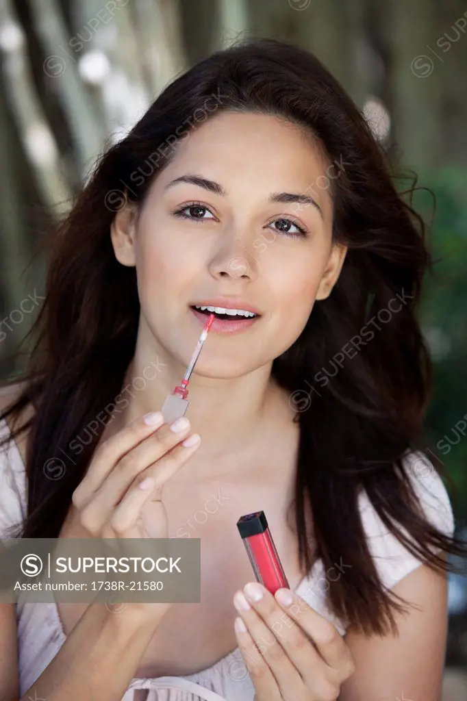 Portrait of a beautiful young woman applying lip gloss