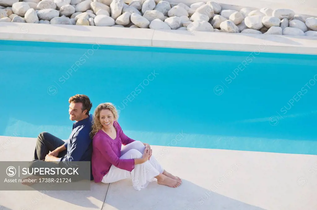 Mid adult couple sitting back to back at the poolside