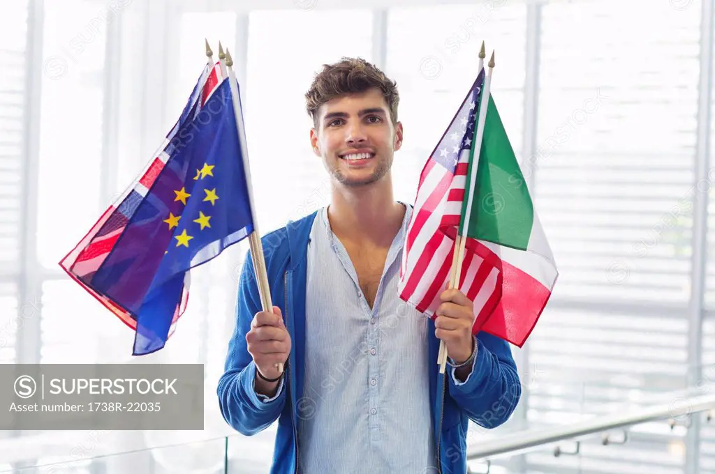 Portrait of a man holding flags of various countries at an airport
