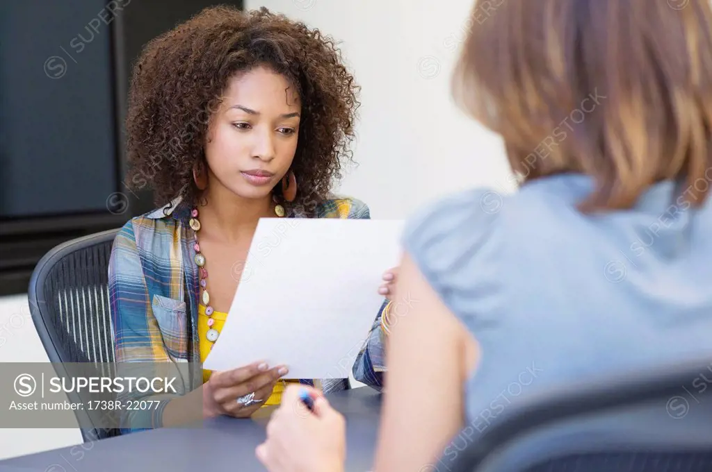 African American woman reading a resume while taking interview of a Caucasian woman
