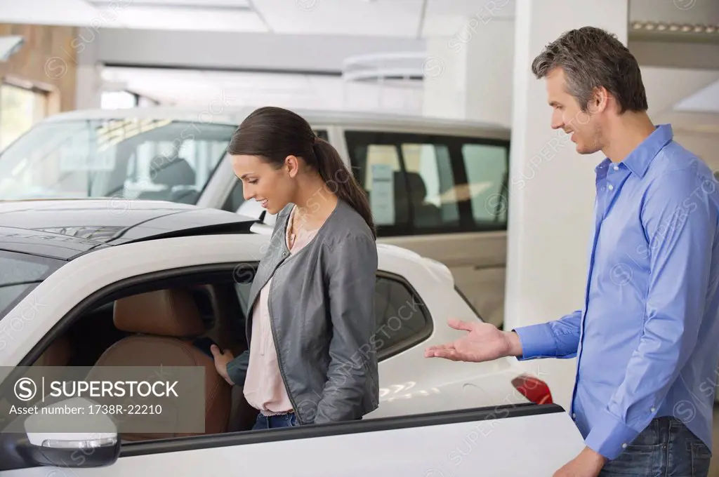 Young woman checking car from inside while man holding the door