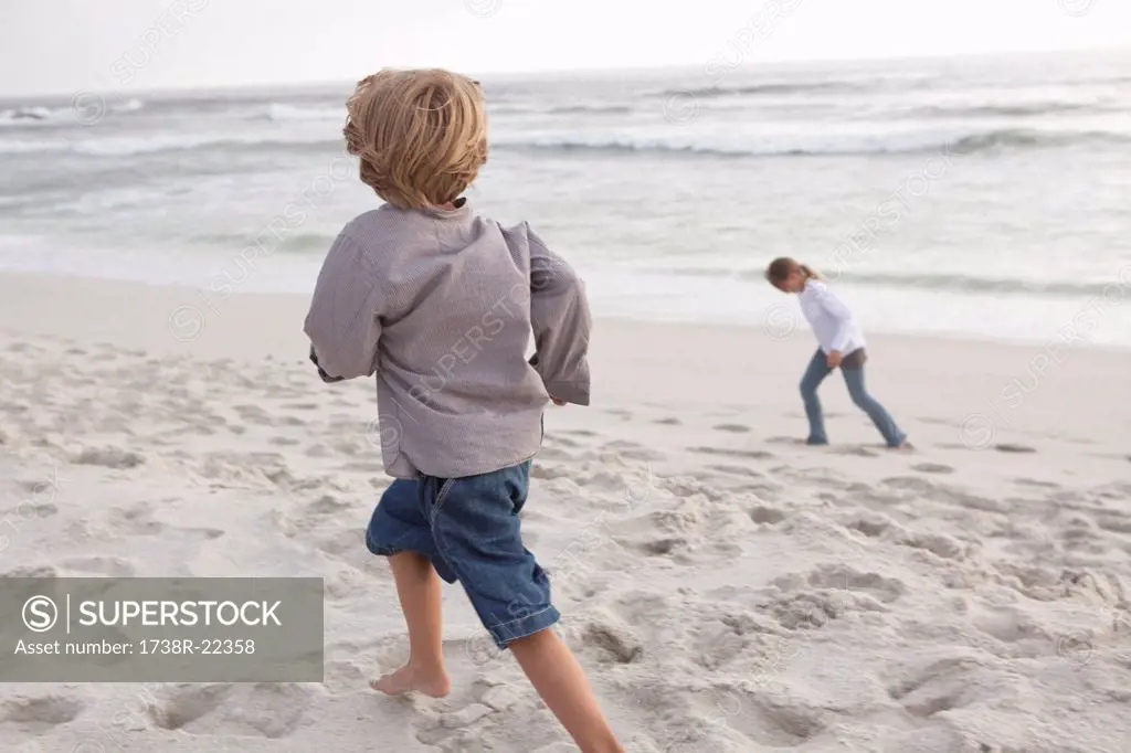 Rear view of a boy running on the beach with his sister