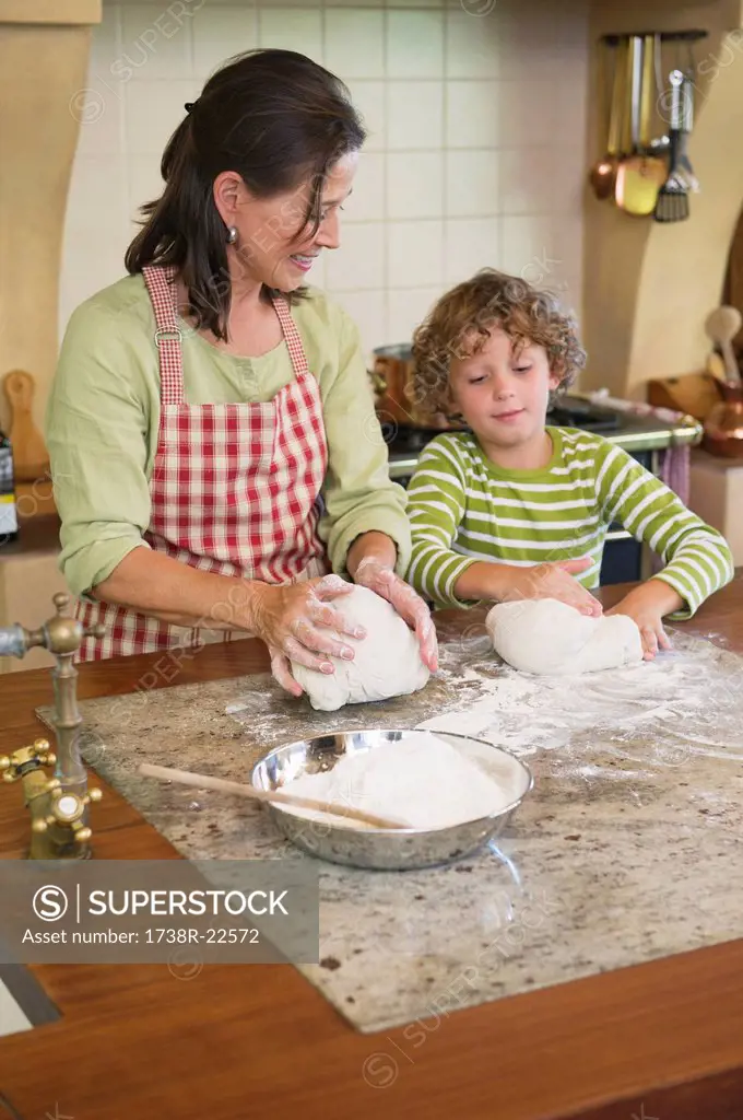 Grandmother and little boy kneading dough at kitchen