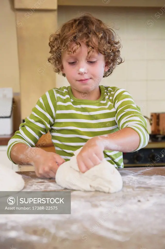 Cute little boy kneading dough at kitchen