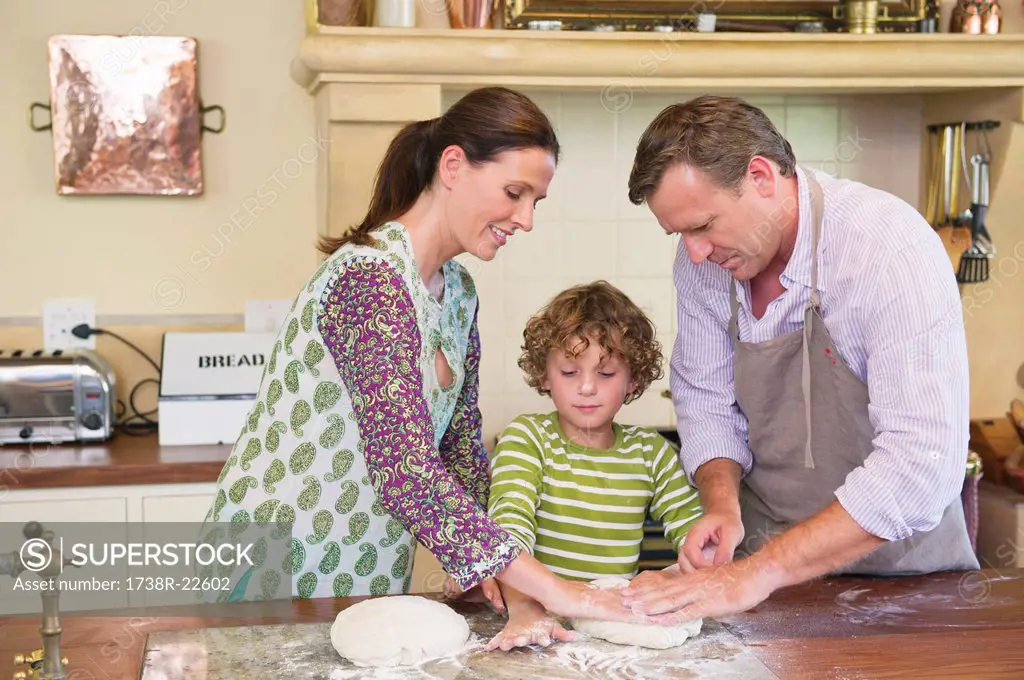 Cute little boy and his parents kneading dough at kitchen