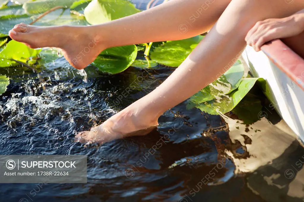 Woman lying in a boat and dipping her legs in a pond