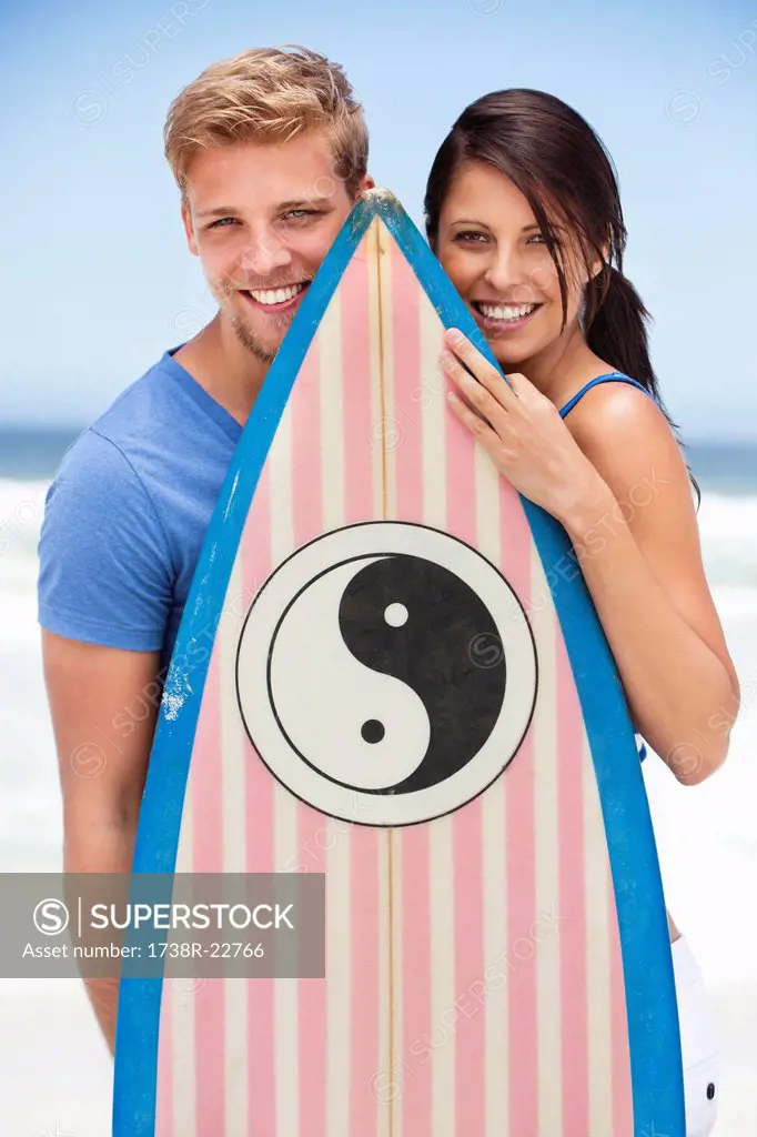 Portrait of a couple standing on the beach with surfboard