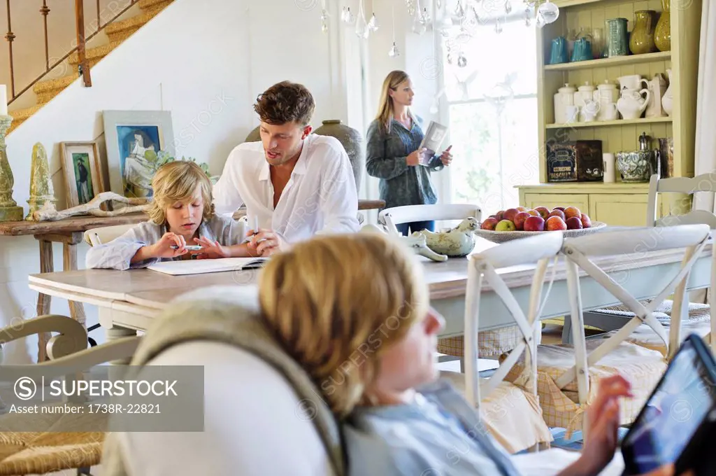 Man teaching little boy while family members busy doing their work at house